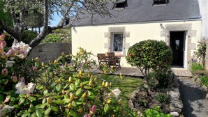 Een huis met een stenen gevel, een kleine tuin met bloeiende planten en een deur naar de entree.