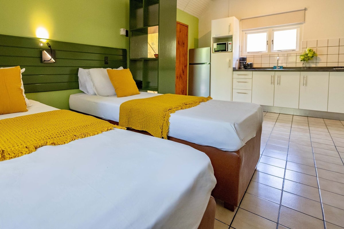 A hotel room with two beds, a kitchenette, and a green wall.