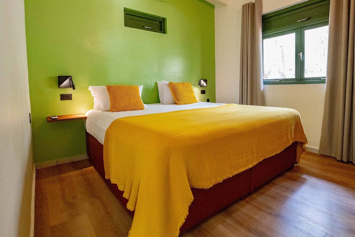 A hotel room with a bed, green walls, wooden flooring, and a window with curtains.