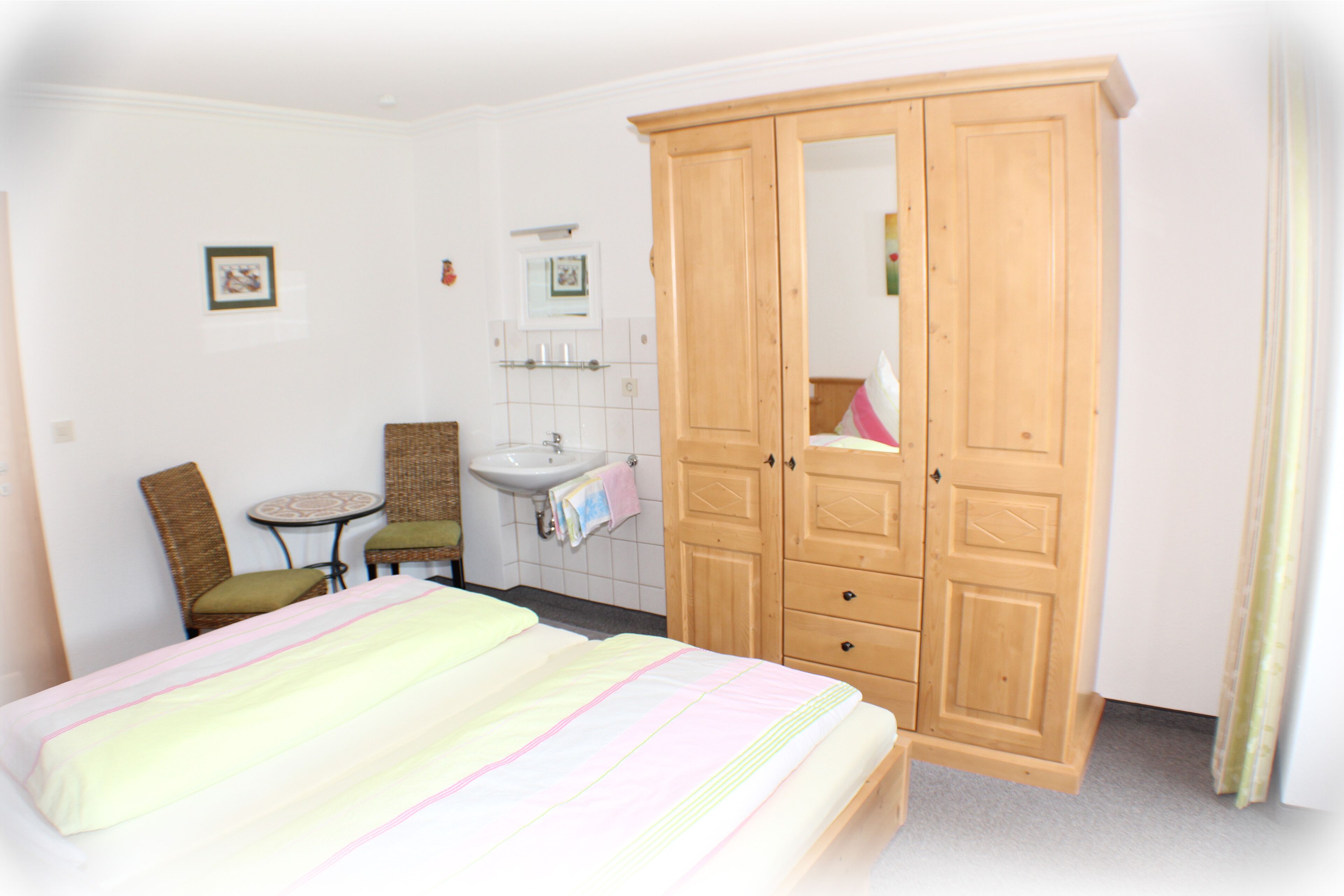 Een hotelkamer met een bed, een houten garderobe, een tafeltje met een stoel, een wastafel en een spiegel.