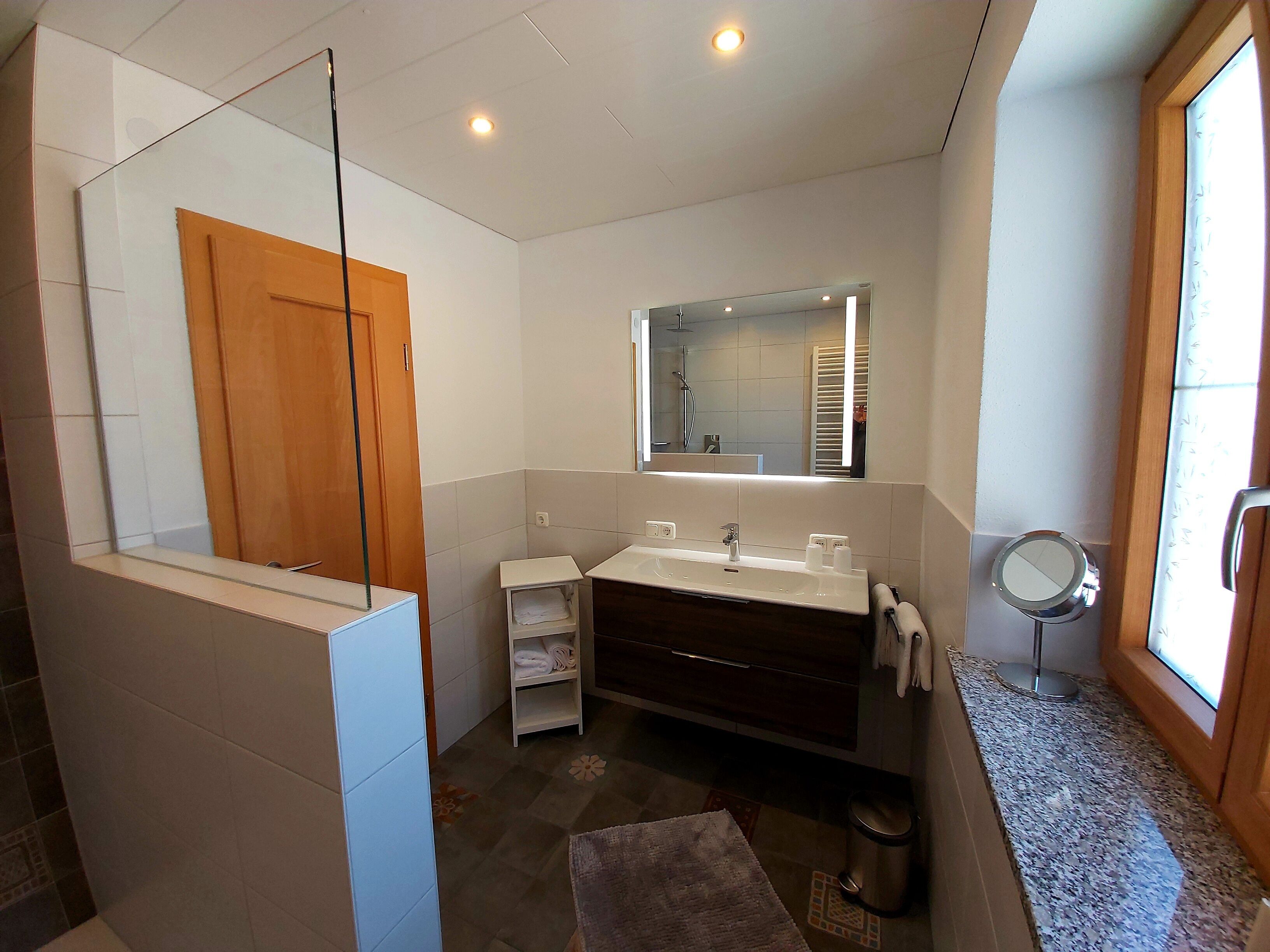 Un bagno moderno con doccia a vetro, un lavabo con specchio e una finestra che offre luce naturale.