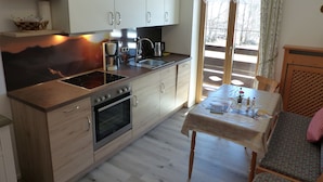 A modern kitchen with a built-in oven, a coffee maker, and a sink. There is a dining table with chairs and a view of the outdoors through a glass door. - Tauernblick vacation apartment - so close to heaven! Maria- Gern, 4 stars. (Berchtesgaden)