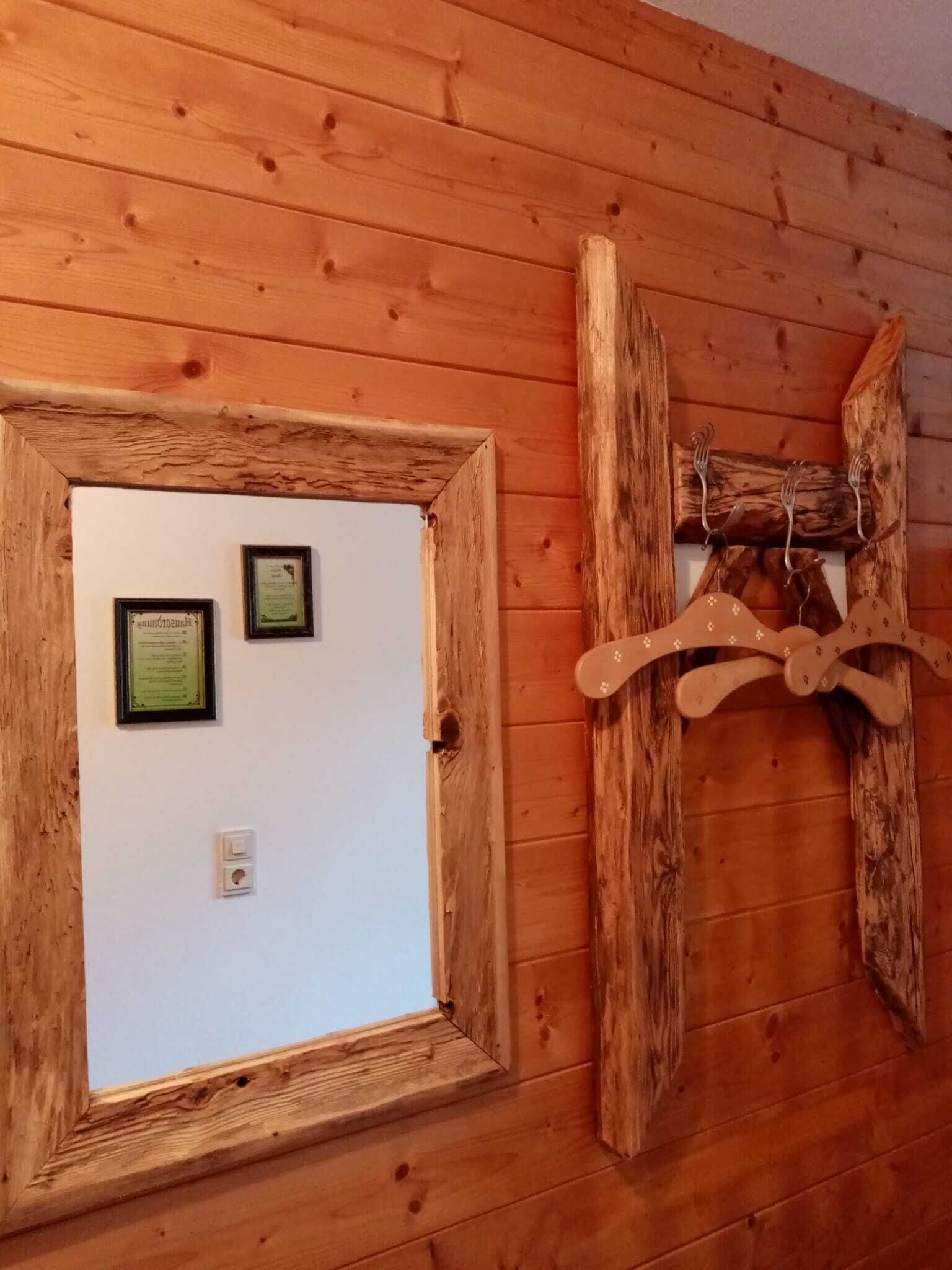 Eine Holzwand mit einem gerahmten Fenster, zwei gerahmten Zertifikaten und einem Holzmantelständer mit Haken.