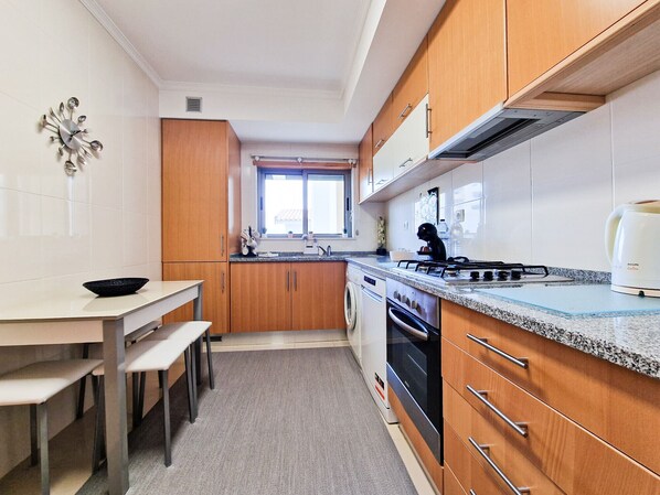 A compact kitchen with wooden cabinets, a gas stove, a built-in oven, and a coffee maker.