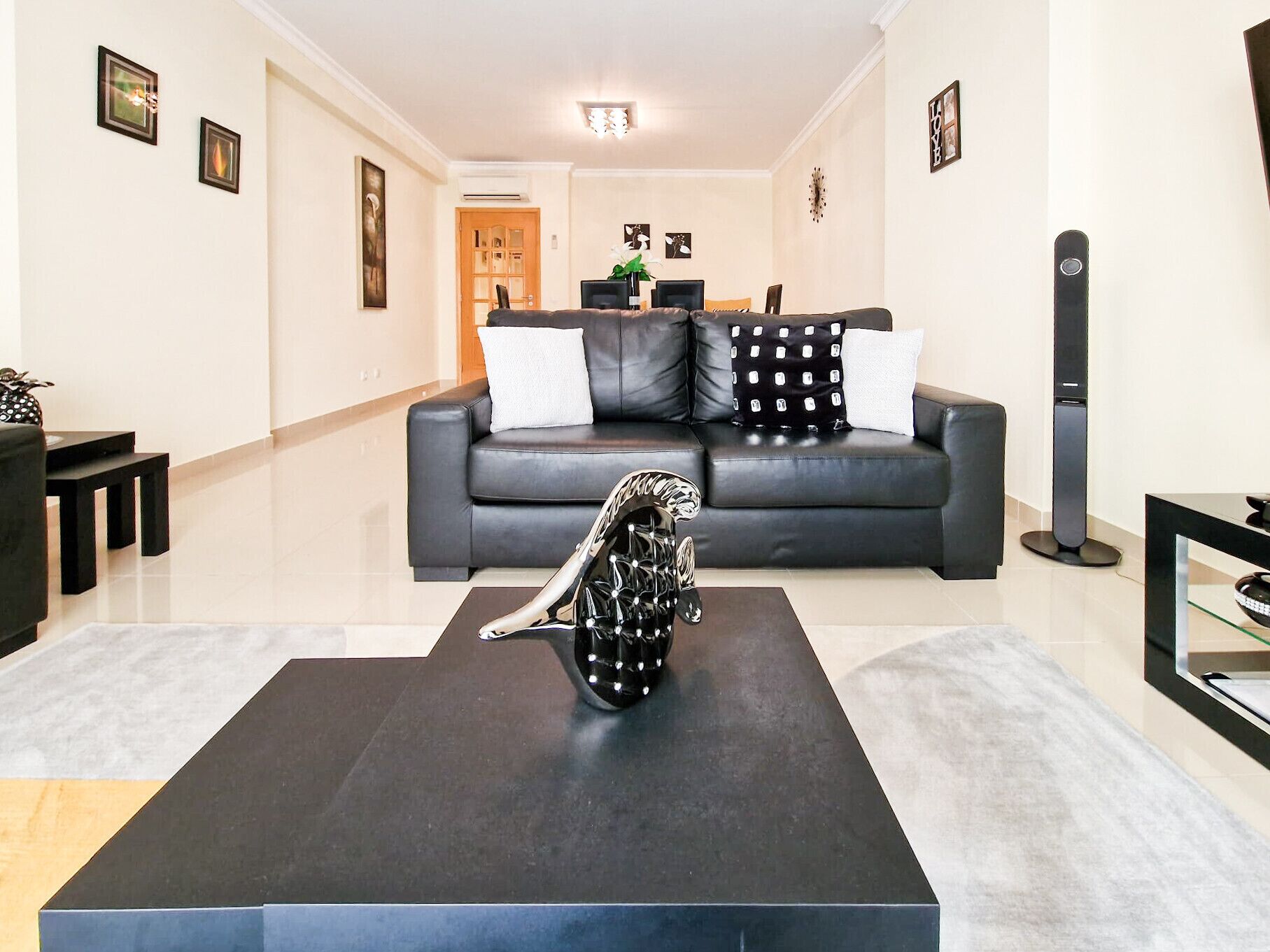 A modern living room with a black leather sofa, a black coffee table with a decorative sculpture, and a black floor lamp.