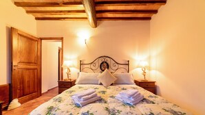 A bedroom with a wooden ceiling, a bed with floral bedding, two bedside lamps, and a nightstand with a lamp. - Podere Vergianoni immersed in Chianti with swimming pool (Noce)