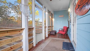 A covered porch with wooden railings, a red chair, and a blue wall with a sign.