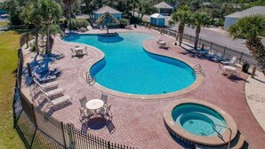 A large, curved swimming pool with lounge chairs and tables around it, surrounded by palm trees and a brick walkway.