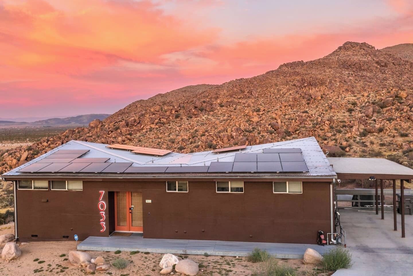 A brown building with solar panels on the roof, a door, and a sign reading "7".