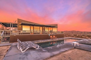 A modern building with a pool, outdoor seating, and a view of the landscape.
