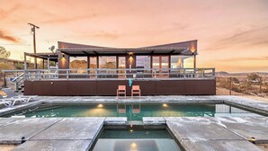 Un área de piscina moderna con un bar con paredes de vidrio y sillas de descanso.
