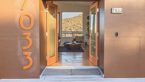 Entrada de un hotel con un cartel con el número '7033' y vista del interior, que incluye una zona de estar y una ventana con vistas a un paisaje rocoso.