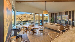 Un amplio salón con un televisor grande, muebles de madera y vistas a un paisaje montañoso.
