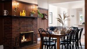 A dining area with a brick fireplace, black chairs, and a table set for six. - Homestead - Picturesque home in an ideal location (Hepburn Springs)