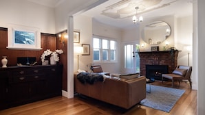 A living room with a fireplace, a sofa, a coffee table, and a TV. There is a wooden cabinet with decorative items and a mirror on the wall. - Homestead - Picturesque home in an ideal location (Hepburn Springs)