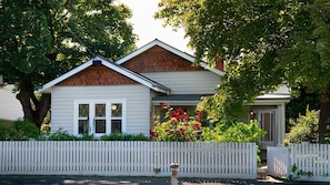 Une maison de plain-pied avec un toit à pignon, un revêtement extérieur blanc et un porche à l’avant orné de fleurs rouges.