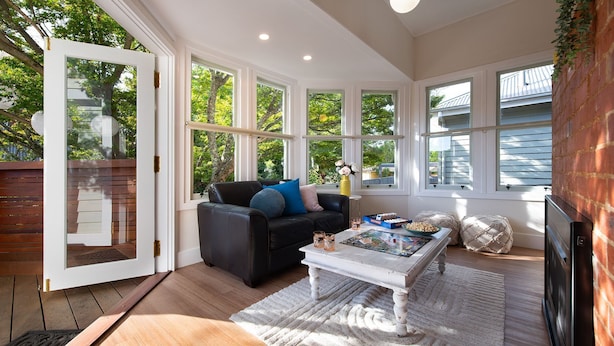 A sunlit room with a black leather sofa, a coffee table with magazines, and a brick wall. - Homestead - Picturesque home in an ideal location (Hepburn Springs)