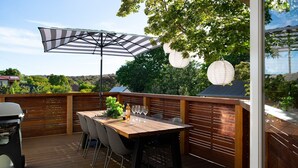 A wooden deck with a table and chairs, a grill, and a large striped umbrella. - Homestead - Picturesque home in an ideal location (Hepburn Springs)