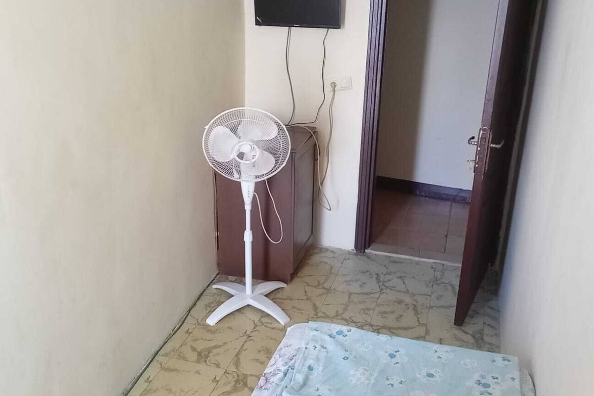 A room with a standing fan, a television mounted on the wall, and a door leading to another room.