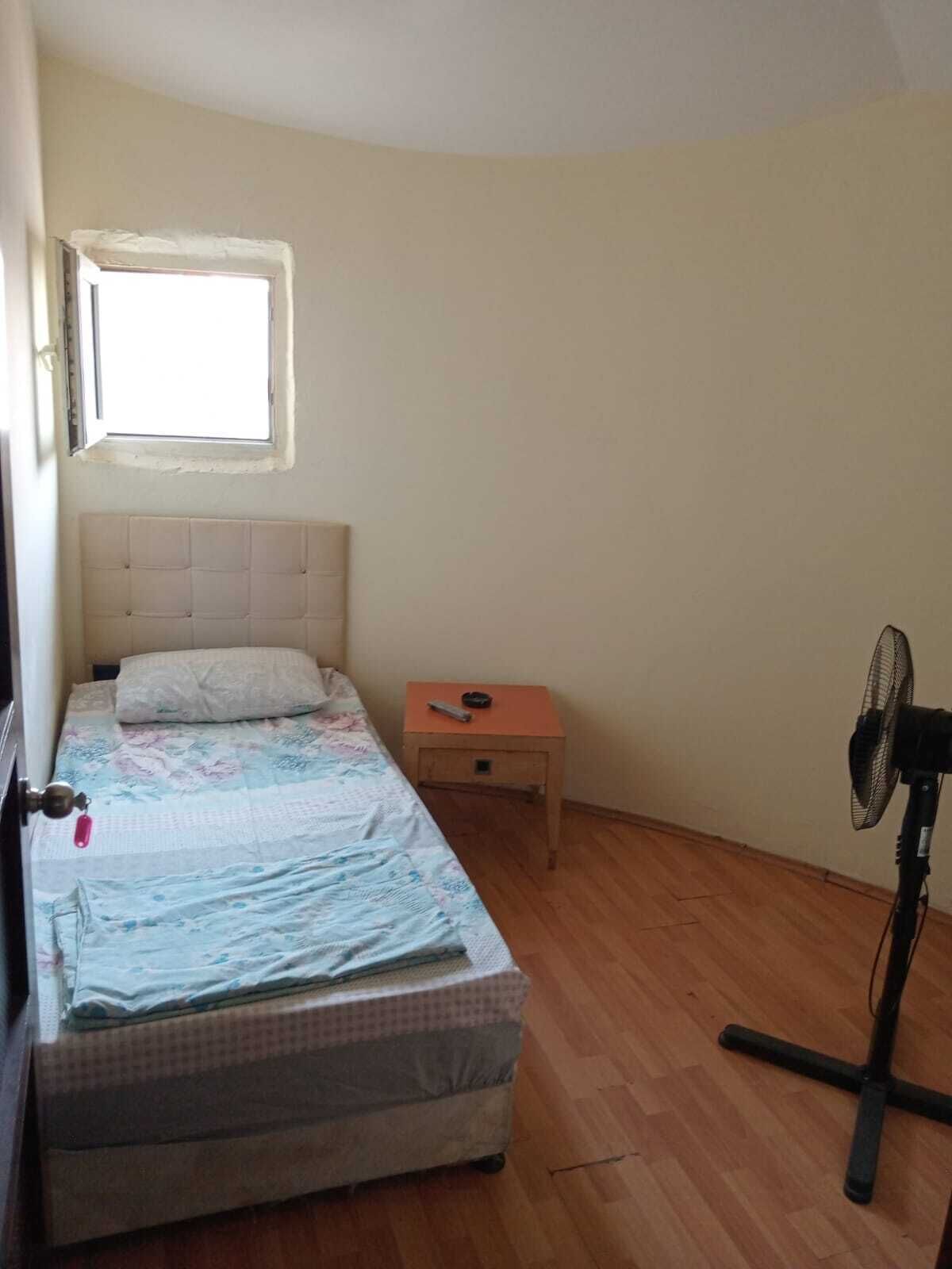 Un dormitorio con cama, mesita de noche, ventilador y ventana.