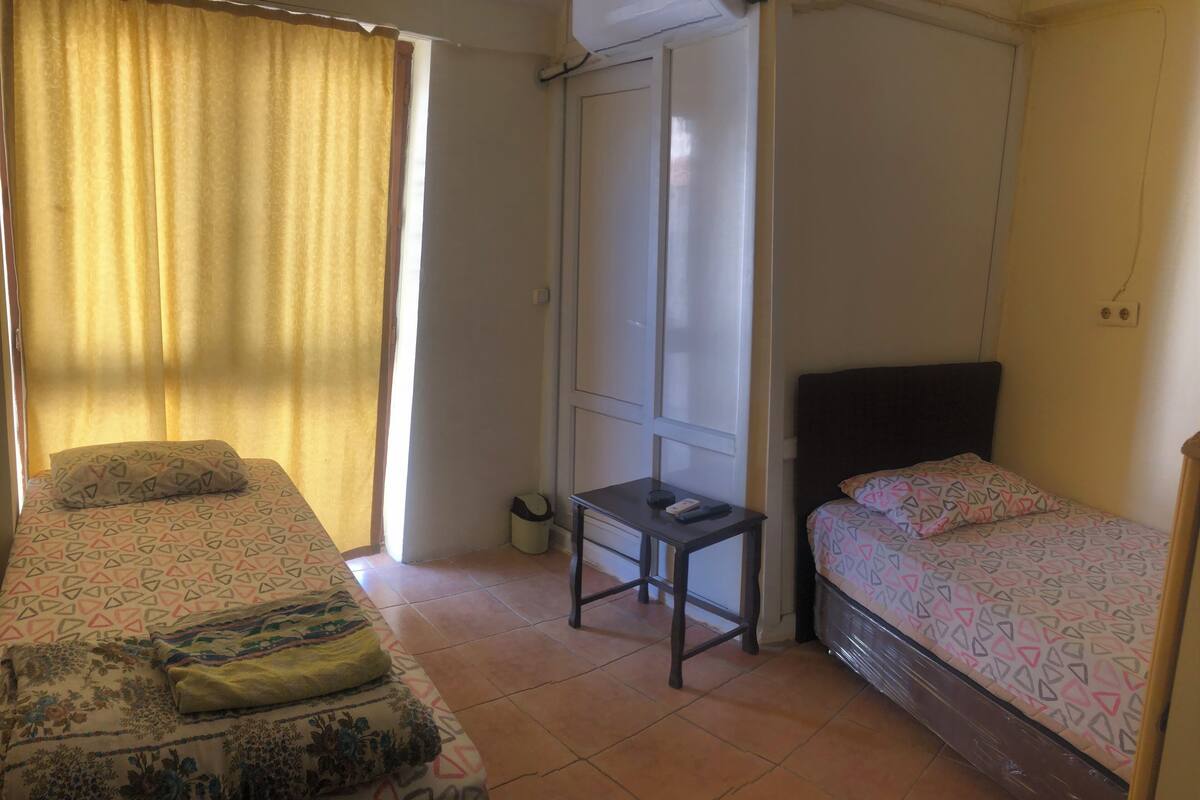A room with two beds, a small table, and a window with curtains.