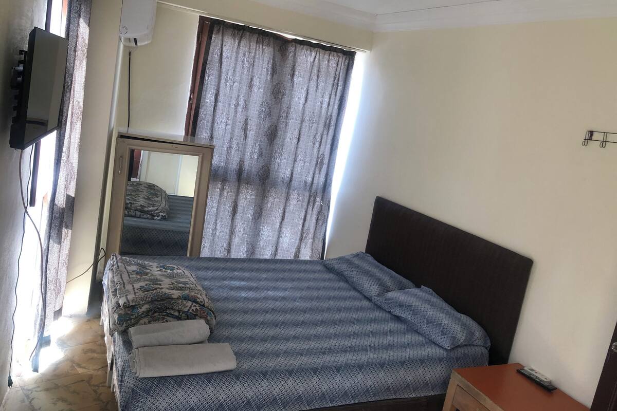 A hotel room with a bed, a small table, a mirror, and a TV mounted on the wall.