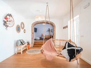 A room with a hanging chair, a wooden bench, a round rug, and a stone archway leading to another room.