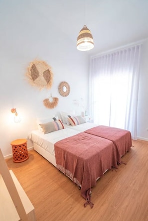 A bedroom with a bed, two bedside tables, a hanging light fixture, and a window with curtains.