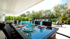 Un espace repas extérieur avec une table à plateau de verre, des chaises en osier et une piscine en arrière-plan.