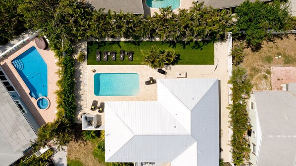An aerial view of a resort with two swimming pools, a grassy area with sun loungers, and a white-roofed building. - Key Royale Gem – Luxury Island Living with Private Heated Pool, pet friendly (Holmes Beach)