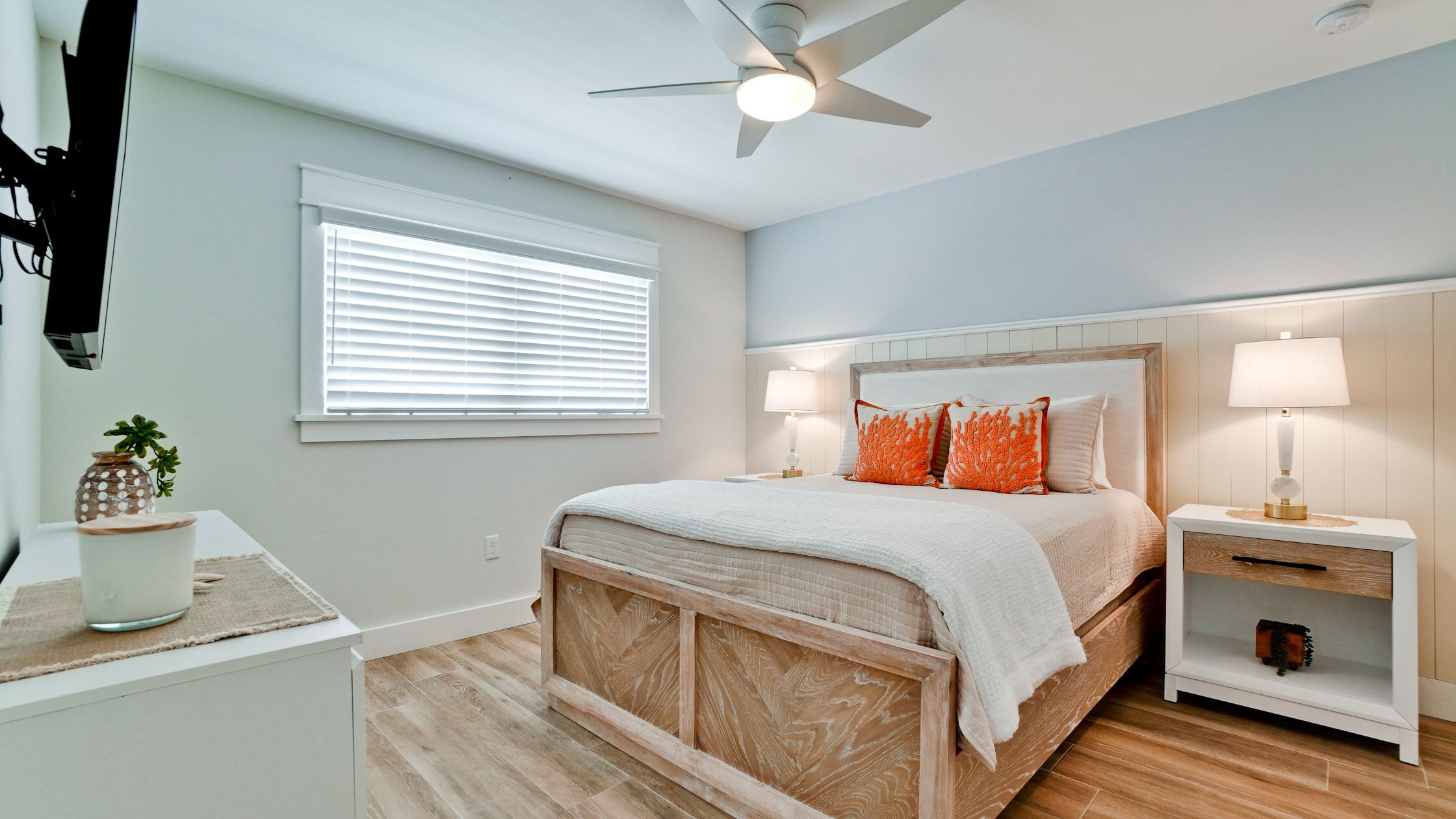Une chambre à coucher comprenant un lit, des tables de chevet, un ventilateur de plafond et une fenêtre avec des stores.