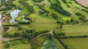 Vue aérienne d’un parcours de golf comportant plusieurs trous, des plans d’eau et une végétation luxuriante environnante.
