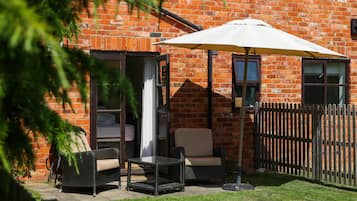 A patio area with wicker furniture, a white umbrella, and a brick wall.