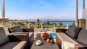 A balcony with wicker furniture, a fruit bowl, and a view of the sea. - Gkountis Deluxe Apartment: Sea View, Shared Pool & Wi-Fi (Lefkadas)