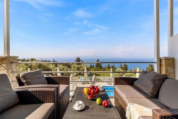 A balcony with wicker furniture, a fruit bowl, and a view of the sea.