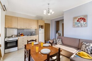 A modern kitchen with wooden cabinets, a dining table set for four, and a sofa in the living area.
