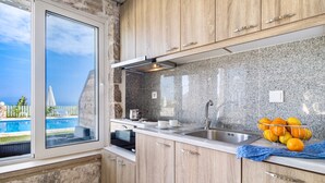 A kitchen with granite countertops, wooden cabinets, a stainless steel sink, and a view of a swimming pool. - Gkountis Stone Apartment 3: Sea View, Shared Pool & Wi-Fi (Lefkadas)