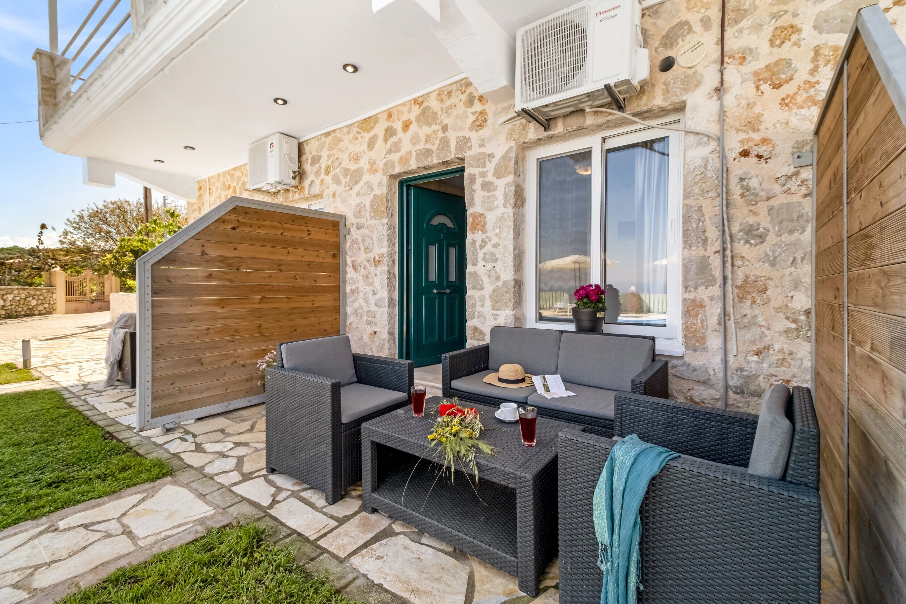 Uma casa de pedra com porta verde, área de estar externa e uma pequena mesa com bebidas e flores.