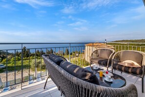 A balcony with wicker furniture, a table with a drink, and a view of the sea.