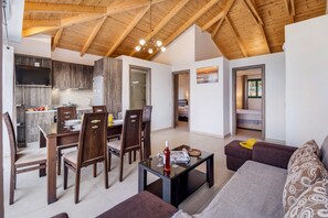 Un intérieur moderne comprenant un coin repas, une cuisine et un espace de vie, avec des poutres en bois, une table basse en verre et un canapé.