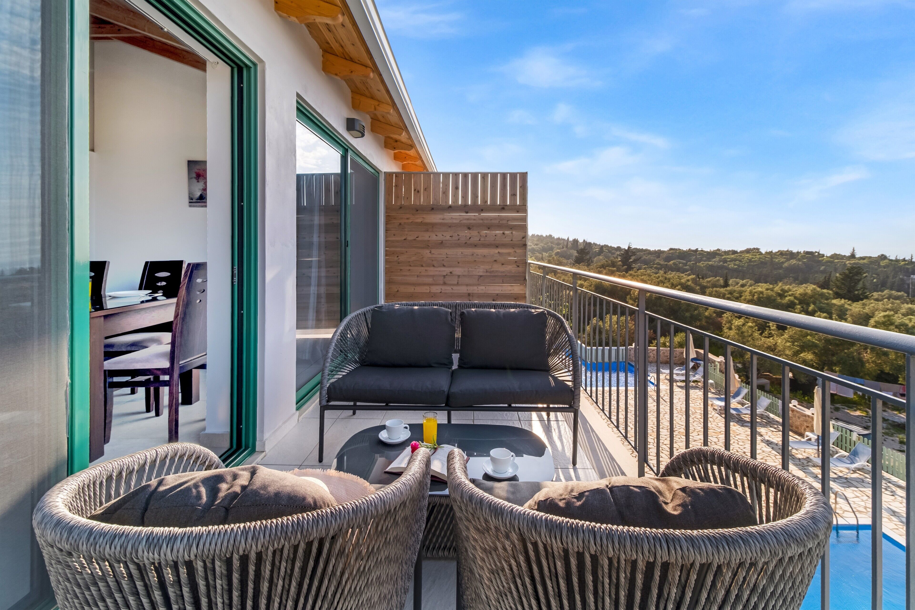 A balcony with wicker furniture, a table with cups and a glass, and a view of the landscape.