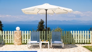 Zona de piscina amb dues cadieres de relax, un parasol blanc i un pilaret de pedra.
