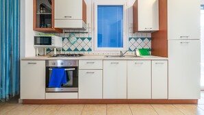 Una cocina con armarios blancos, microondas, estufa y ventana con persianas.