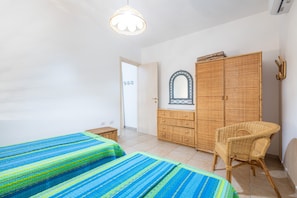 Une chambre avec deux lits, une chaise en osier, une armoire et un miroir.