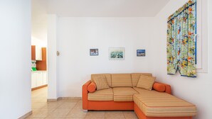Una sala moderna con un sofá seccional, un comedor con armarios y una cocina visible a través de un vano abierto.