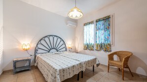 Un dormitorio con cama, lámparas de noche, una silla y una ventana con cortinas.