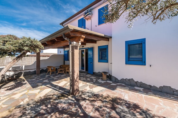 Une maison avec une terrasse en pierre, une pergola en bois et une porte bleue.