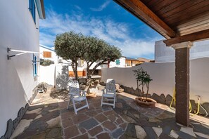 A courtyard with stone flooring, two white chairs, a tree, and a hose. - Holiday Home "Sottotorre 1" close to the Sea with Private Garden & A/C (Calasetta)