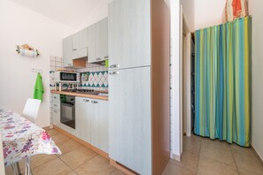 Eine kompakte Küche mit Mikrowelle, Herd und Backofen, ein Esstisch mit Blumenmuster-Tischdecke und ein grüner Stuhl.