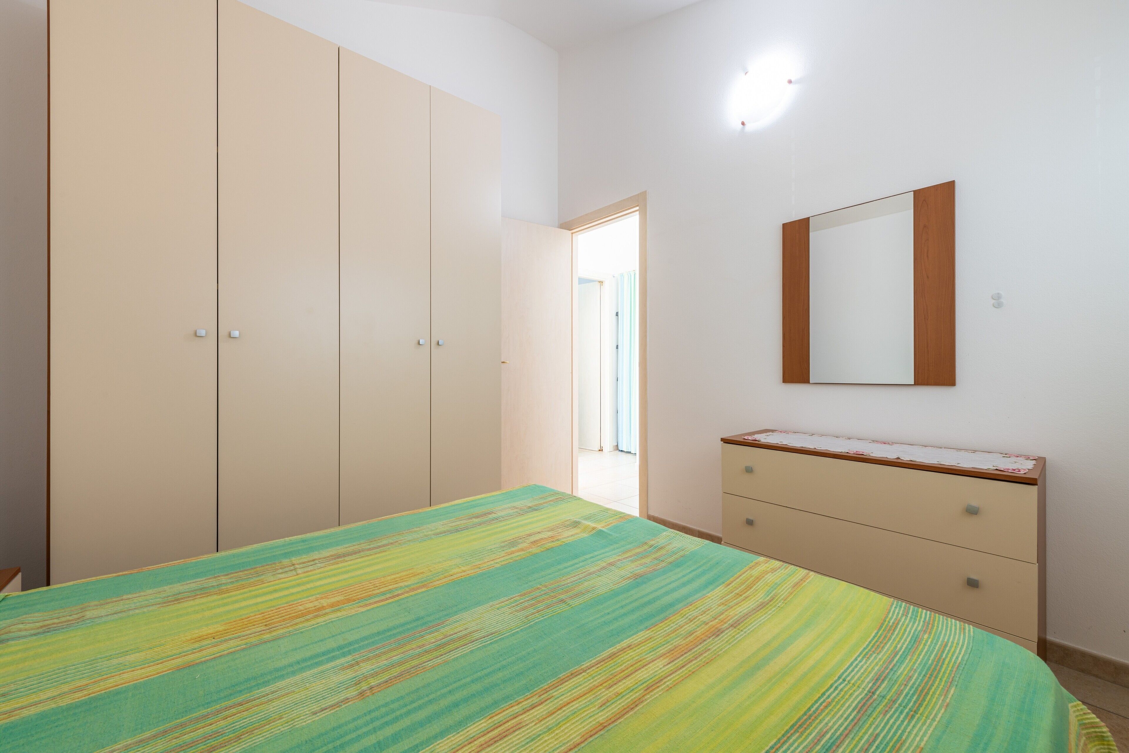 Un dormitorio con cama, armario, cómoda y espejo.
